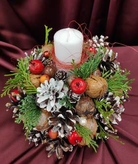 Pokaż zdjęcie: stroik świąteczny wykonany z szyszek, orzechów włoskich, igliwia na środku biała świeca.