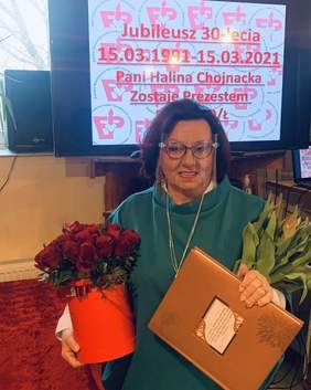 Pokaż zdjęcie: na zdjęciu: Halina Chojnacka Prezes Stowarzyszenia PSLCnP Oddział Łódzki trzyma pamiątkowy dziennik i kwiaty