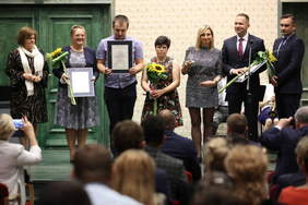 Pokaż zdjęcie: Grupa kobiet i mężczyzn ze statuetkami, dyplomami w ramach i słonecznikami stojąca na scenie Filharmonii