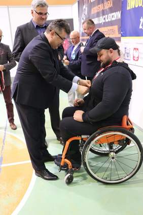Pokaż zdjęcie: Sekretarz Stanu w Ministerstwie Energii Grzegorz Tobiszowki wręcza pamiątkowy medal niepełnosprawnemu zawodnikowi