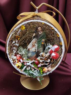 Pokaż zdjęcie: na stojaku wisi bombka w środku bombki dekoracja św Józef, Maryja trzyma dzieciątko.