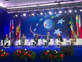 Scena, na niej na krzesłach siedzą paneliści