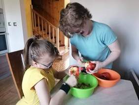 Pokaż zdjęcie: Dwie uczestniczki ŚDS podczas zajęć kulinarnych w domu  - obierają jabłka, 