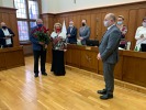 Pokaż zdjęcie: na środku sali obrad stoi Marszałek Województwa Cezary Całbecki, po jego prawej stronie - na górze zdjęcia) stoją 2 osoby z bukietem róż