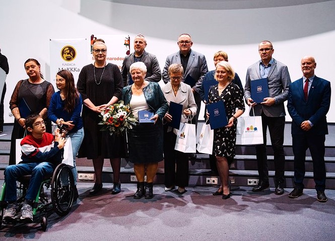 Na scenie stoi grupa osób, nagrodzona upominkami i kwiatami.