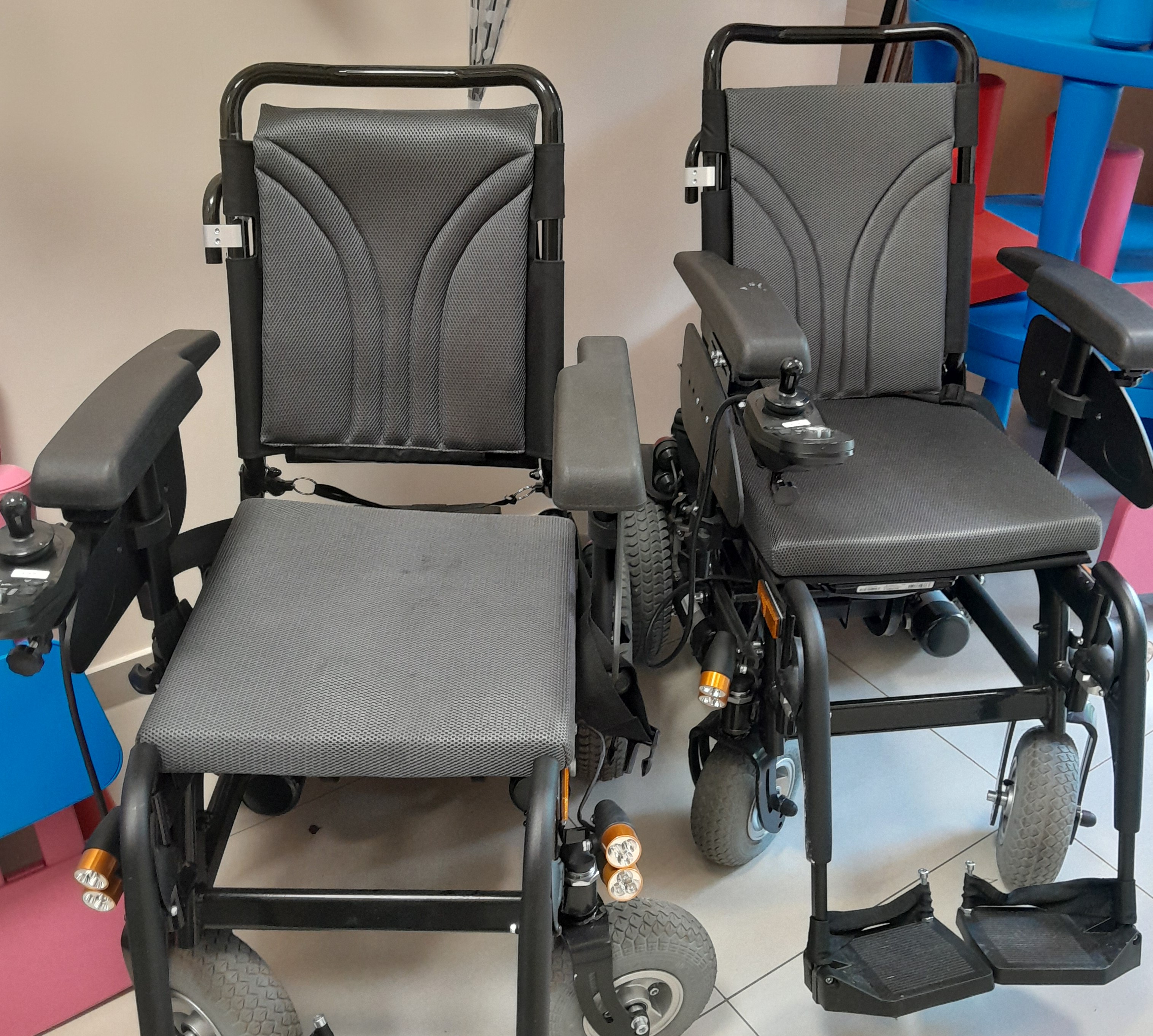 Terenowe wózki inwalidzkie. Dwa terenowe wózki inwalidzkie stojące w pomieszczeniu.