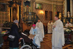 W kościele podczas nabożeństwa, duchowny pochyla się nad osobą na wózku inwalidzkim