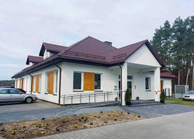 Pokaż zdjęcie: Zdjęcie parterowego budynku w kolorze bezowym z podjazdem dla wózków inwalidzkich