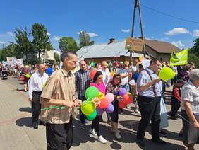 Pokaż zdjęcie: Grupa osób idących z kolorowymi balonami, kwiatami i transparentami.