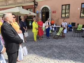 Pokaż zdjęcie: Na rynku starego miasta stoi grupa kobiet i mężczyzn, zdjęcie zrobione podczas otwarcia targów.