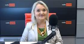 Kobieta ubrana w jasny żakiet z łańcuszkiem na szyi na tle logo Radia Zachód