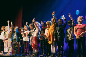 Pokaż zdjęcie: Zdjęcie sceny, na której występuje grupa śpiewających przedszkolaków.