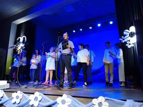 Pokaż zdjęcie: Zespół ludzi na scenie podświetlonej niebieskim światłem