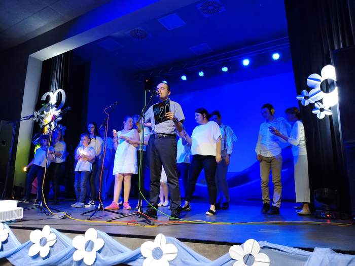 Pokaż zdjęcie: Zespół ludzi na scenie podświetlonej niebieskim światłem