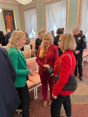 Pokaż zdjęcie: Trzy kobiety stoją zwrócone do siebie. Jedna z kobiet ubrana jest w zieloną marynarkę, druga blondynka z długimi włosami w czerwony garnitur, trzecia kobieta ma czerwoną marynarkę. Sala w Trybunale Koronnym.