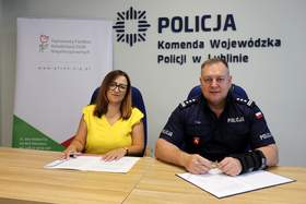Przedstawiciel PFRON i funkcjonariusz Policji podpisują dokumenty przy stole w siedzibie Komendy Wojewódzkiej Policji w Lublinie, na tle logotypów instytucji.