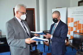 Pokaż zdjęcie: Dwóch mężczyzn w garniturach wymienia się dokumentami. 