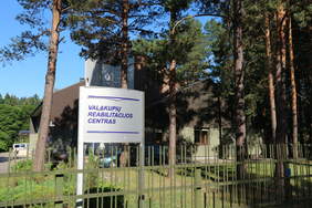 Pokaż zdjęcie: Widok ogólny na Centrum Rehabilitacji Valakupiai z tablicą informacyjną. Ośrodek położony jest w leśnej scenerii.
