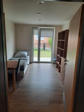 Pokaż zdjęcie: Na zdjęciu znajduje się pokój. Po lewej stronie stoi łóżko i biurko z krzesłem. Po prawej stronie jest regał i komoda. Na wprost widać duże okno.  