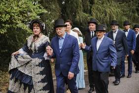 Pokaż zdjęcie: Zdjęcie kobiet i mężczyzn w parach tańczących poloneza, część osób jest przebrana w XIX wieczne stroje, panowie mają kapelusze.