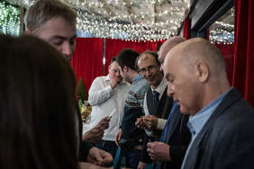 Pokaż zdjęcie: Sześciu mężczyzn składa sobie życzenia i dzieli się opłatkiem.