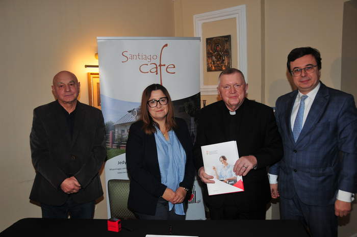 Pokaż zdjęcie: Do pamiątkowego zdjęcia pozują cztery osoby, kobieta, ksiądz oraz dwóch mężczyzn. Ksiądz trzyma w ręku podpisana umowę.