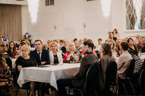 Pokaż zdjęcie: Zdjęcie osób zaproszonych na jubileusz PSONI, siedzących za stołami, przykrytymi białymi obrusami.