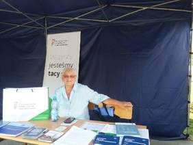 Pokaż zdjęcie: Kobieta siedząca przy stoliku z materiałami informacyjnymi - Radom