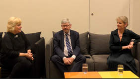 Pokaż zdjęcie: Na kanapach siedzą dwie kobiety i mężczyzna. Rozmawiają ze sobą. Wszyscy są elegancko ubrani. 