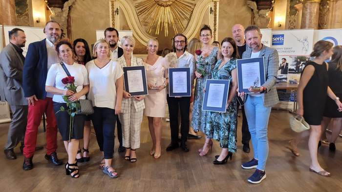 Pokaż zdjęcie: Zdobywcy Lodołamacze stoją obok siebie do zdjęcia grupowego, w sali Oratorium, wypełnionej pozłacanymi zdobieniami