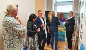 Pokaż zdjęcie: Członkowie Komisji oraz dyrektor Marta Mordarska oglądają prace zgłoszone w kategorii "Malarstwo i witraż". Prace wyeksponowane są na sztalugach oraz ułożone wzdłuż korytarza 