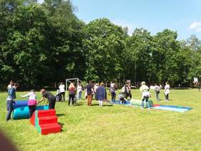 Pokaż zdjęcie: Grupa dzieci i dorosłych pokonujących przeszkody na terenie boiska