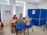W sali NFZ w Lublinie przy stoliku siedzą cztery osoby. Na stole leżą ulotki. Za stolikiem stoi roll-up z logo Centrum Informacyjno-Doradczego dla Osób z Niepełnosprawnościami.