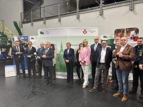 Pokaż zdjęcie: Przy mikrofonie przemawia jeden z uczestników inauguracji wydarzenia, obok stoją przedstawiciele organizatorów oraz zaproszeni goście. W tle widoczne są banery Powiatowego Urzędu Pracy w Elblągu i Miasta Elbląg.