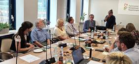 Pokaż zdjęcie: Osoby siedzące przy stole prowadzą rozmowę z ekspertką z Państwowego Funduszu Rehabilitacji Osób Niepełnoprawnych.