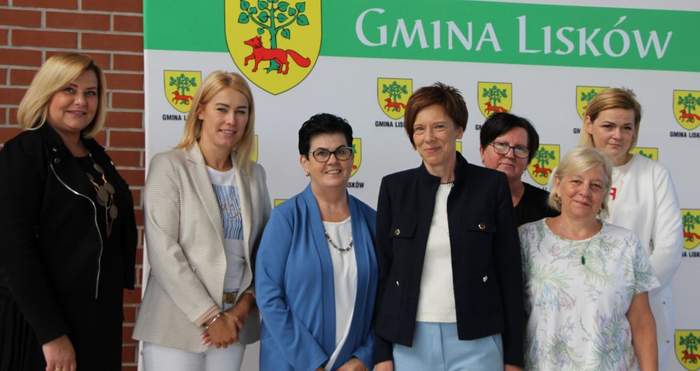 Pokaż zdjęcie: Grupa siedmiu kobiet stoi na tle baneru Gminy Lisków. Na banerze widoczny jest herb gminy.