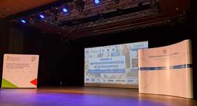 Scena, a na niej stoją ścianki PFRON-u i PIP-y, w tle ekran z wyświetlonym tytułem konferencji oraz nazwami organizatorów i patronatów