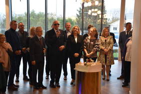 Uczestnicy uroczystości, stoją na tle okien w hotelu, przed nimi tort