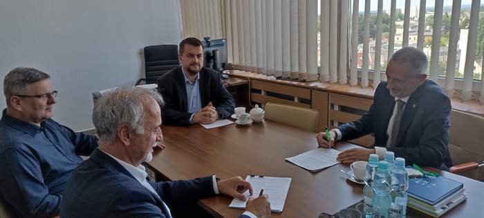 Pokaż zdjęcie: Przy stoliku siedzą czterej mężczyźni, którzy podpisują umowę o dofinansowanie auta, wszyscy są ubrani na galowo