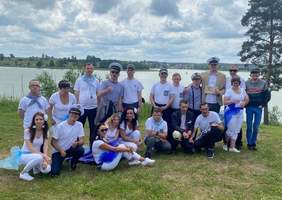 Pokaż zdjęcie: Na pierwszym planie kobieta trzyma w rękach mikrofon i śpiewa, po lewej i prawej stronie stoją banery reklamujące PFRON i Ryn, za nią 6 osób macha niebieskimi i białymi kawałkami materiałów