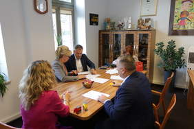 Pokaż zdjęcie: Przy stole konferencyjnym z Pełnomocnikami Zarządu Wejherowskiego siedzą Dyrektor Oddziału PFRON ubrany w białą koszulę, krawat i granatową marynarkę trzymający pióro w lewej dłoni, w prawej żółtą pieczątkę oraz pełnomocnik PFRON – si