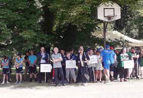 Pokaż zdjęcie: Stojąca grupa zawodników z tabliczkami, na których znajdują się nazwy placówek