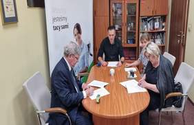 Pokaż zdjęcie: na zdjęciu pomieszczenie Oddziału, po środku stoi duży stół  przy którym siedzą osoby i podpisują dokumenty 