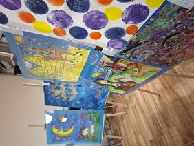 Przestronna sala. Wzdłuż ścian rozmieszczono wiele obrazów na sztalugach, krzesłach.