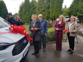 Pokaż zdjęcie: Na zdjęciu nowy bus z czerwoną wstęgą na masce, obok goście przybyli na uroczyste przekazanie busa