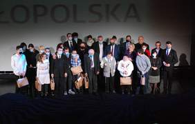 Pokaż zdjęcie: Scena "Opery Krakowskiej". Na scenie stoją laureaci konkursu, osoby wręczające nagrody oraz komisja konkursowa. Laureaci trzymają nagrody.  