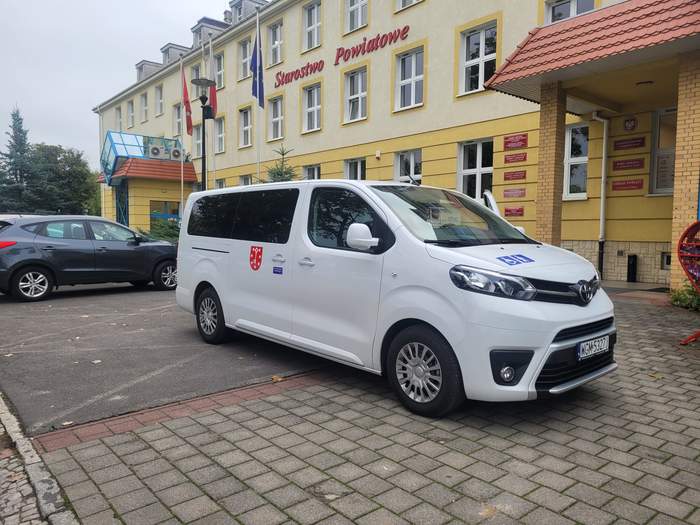 Pokaż zdjęcie: Mikrobus do przewozu osób z niepełnosprawnościami stoi przed budynkiem Starostwa w Gorzowie Wlkp., auto jest koloru białego