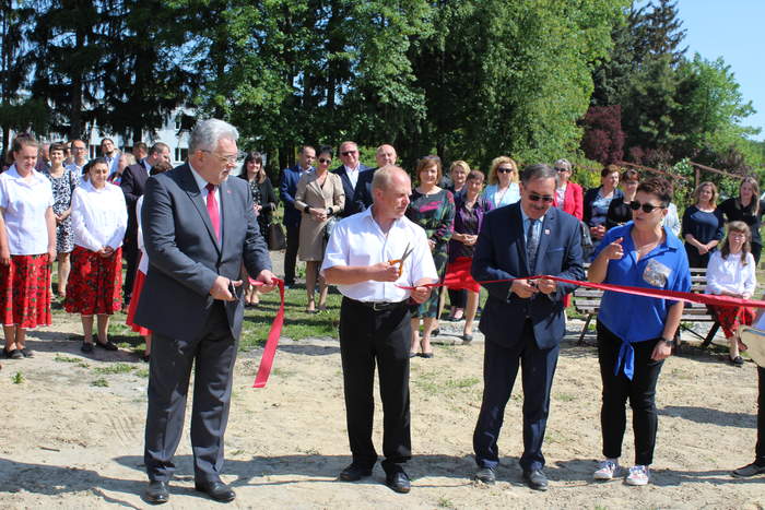 Pokaż zdjęcie: Trzech mężczyzn przecina czerwoną wstęgę, zdjęcie w plenerze, z tyłu duża grupa ludzi 