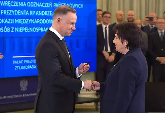 Pokaż zdjęcie: Danuta Tarnawska odbiera odznaczenia od Prezydenta RP, w tle niebieska plansza, wszyscy ubrani na galowo