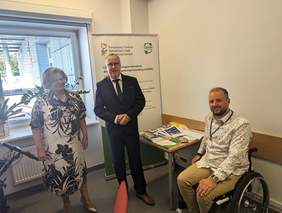 Pomieszczenie nowego punktu zamiejscowego CIDON w BYdgoszczy, od lewej stoją:Dyrektor Kujawsko-Pomorskiego Oddziału PFRON - Aleksandra Gierej, obok Dyrektor Oddziału ZUS w Bydgoszczy - Mariusz Jaroniewski oraz siedzi na wózku inwalidzkim pracownik punktu CIDON - Paweł Dzik. W tle baner dot, CIDON-u 